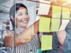 Eine Frau und ein Mann kleben Post-Its auf eine Glaswand