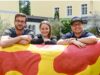 Drei junge Menschen lehnen über einer Figur und lächeln.