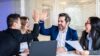 4 Personen sitzen lachend an einem Tisch und zwei Personen geben sich ein High-Five